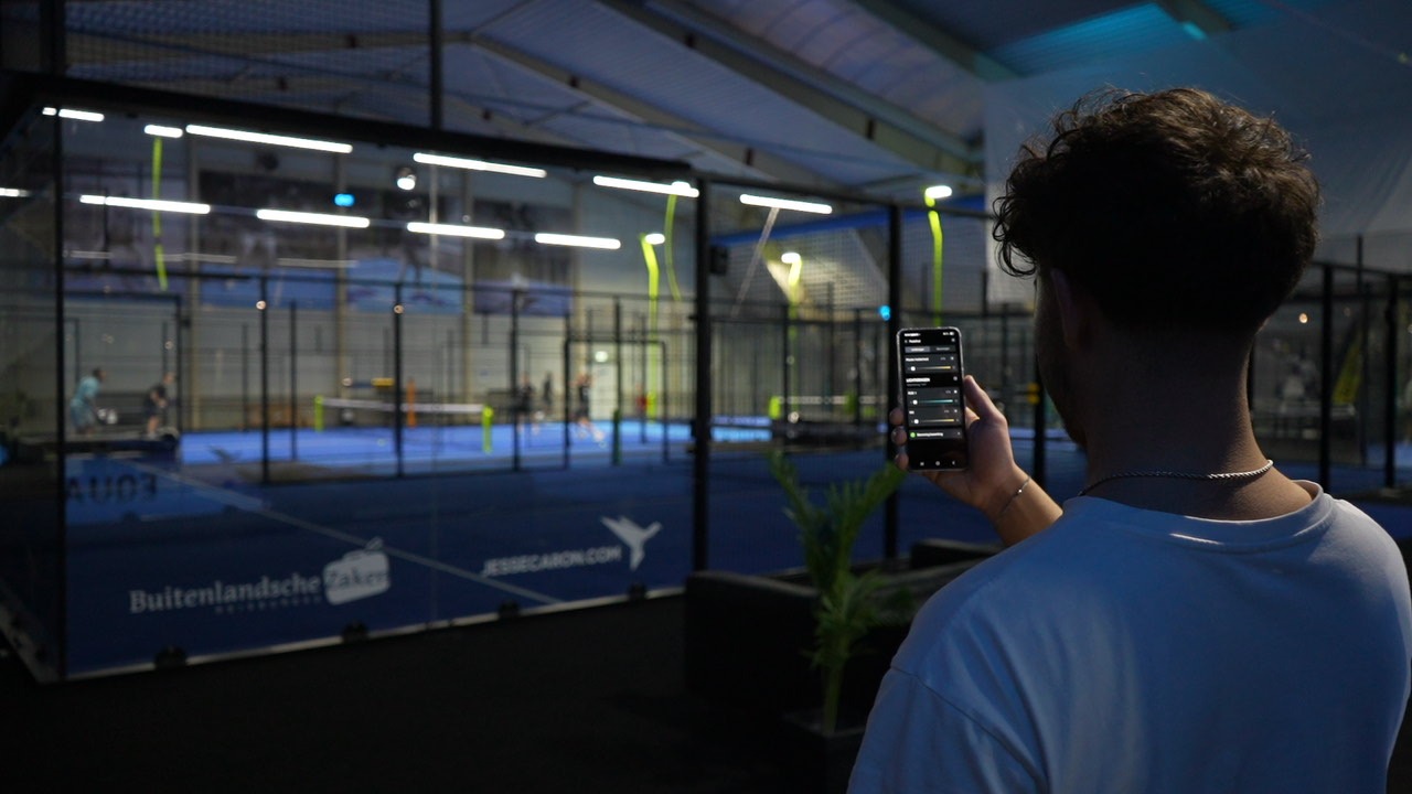 Iemand bedient met een smartphone de techniek bij de padelbanen