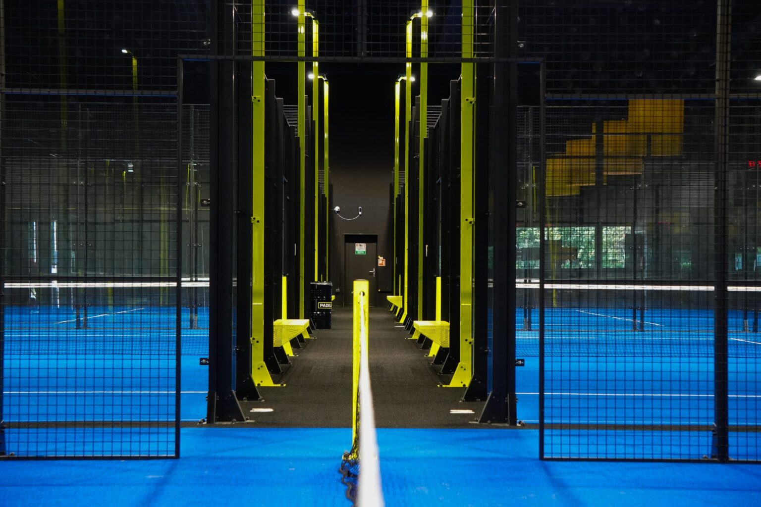 Verlichte indoor padelbanen met blauwe speelvelden en een centrale doorgang