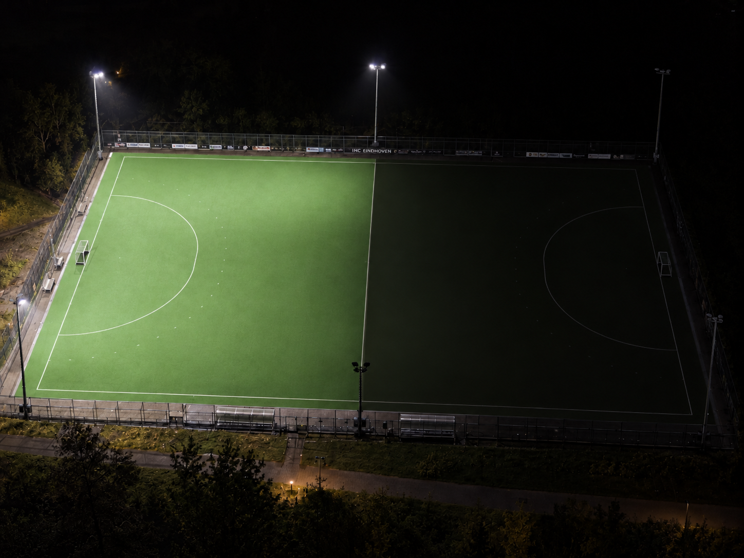 Hockeyveld in de avond, vanuit de lucht gefotografeerd met één verlichte veldhelft