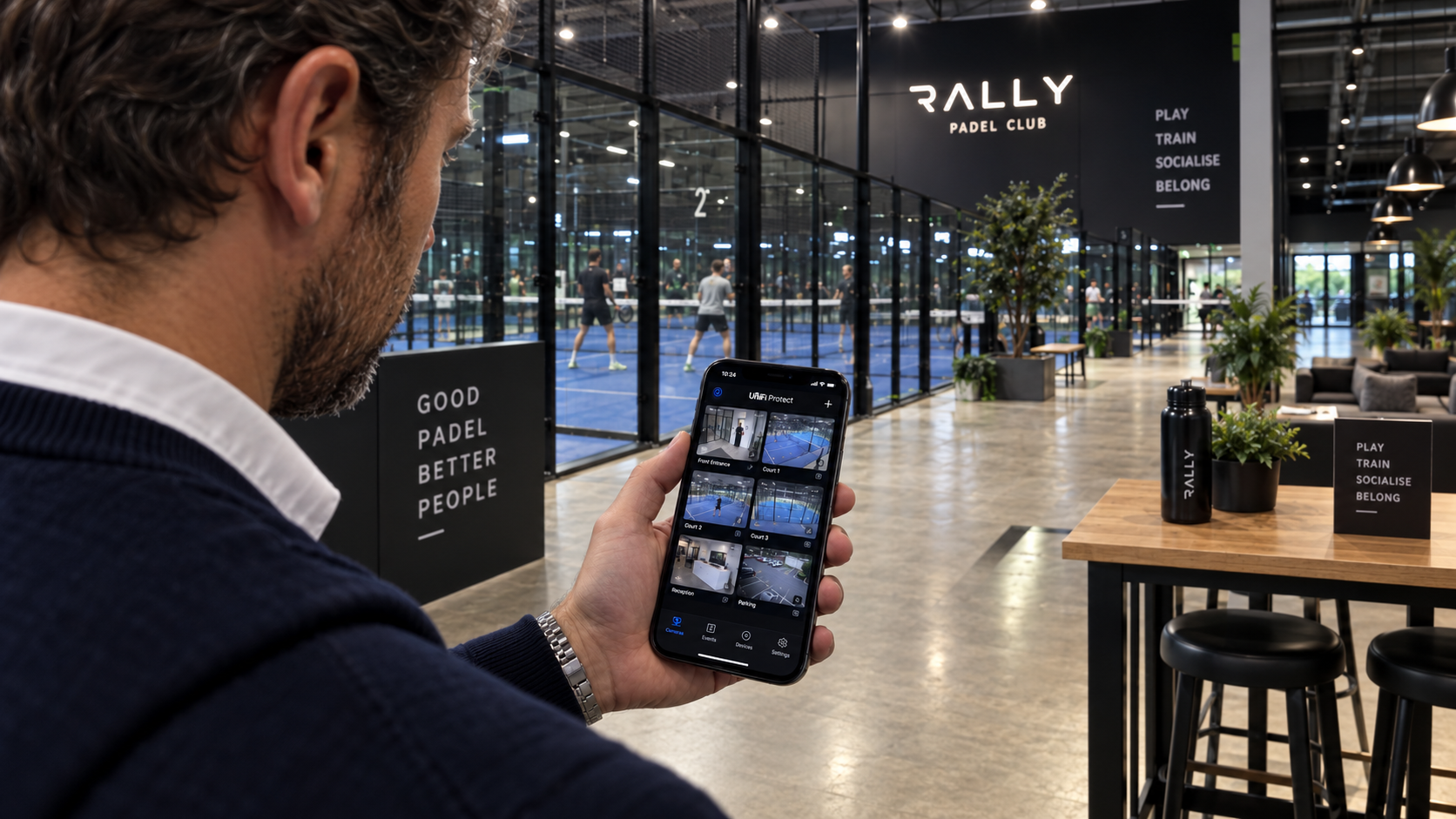 Een persoon bekijkt camerabeelden op een smartphone in een moderne padelclub
