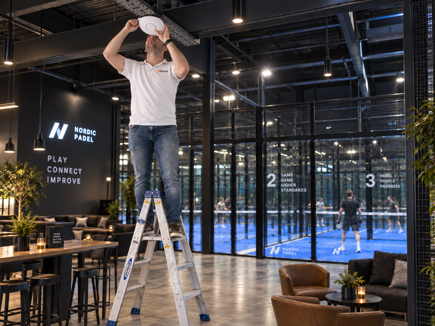Een technicus op een ladder installeert een wifi-accesspoint in een padelclub